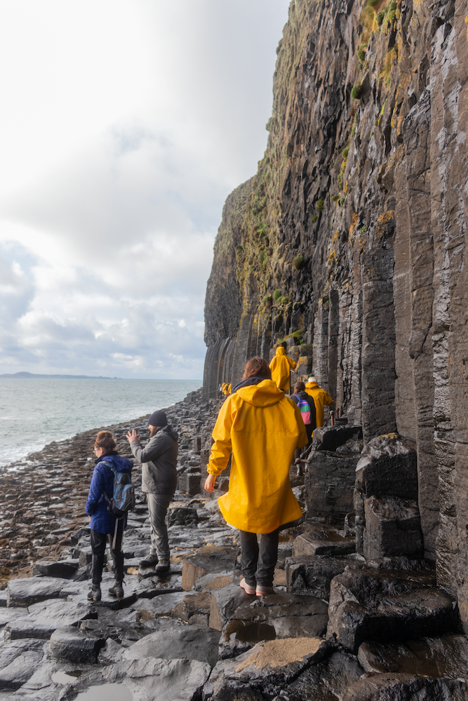 Person in yellow rain jacket walking beside rocky cliff